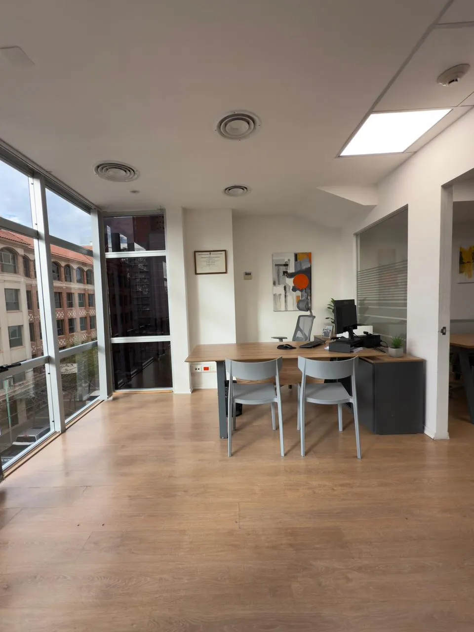Escritorio principal de madera frente a un gran ventanal con vista urbana, ambiente luminoso y profesional.