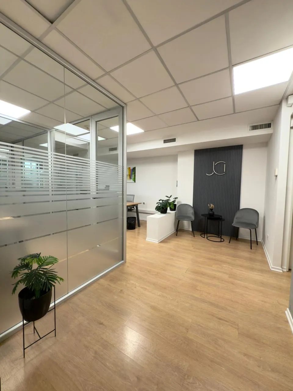 Vista amplia de la recepción del estudio jurídico con logo JI en panel gris, pisos de madera y mamparas de vidrio.
