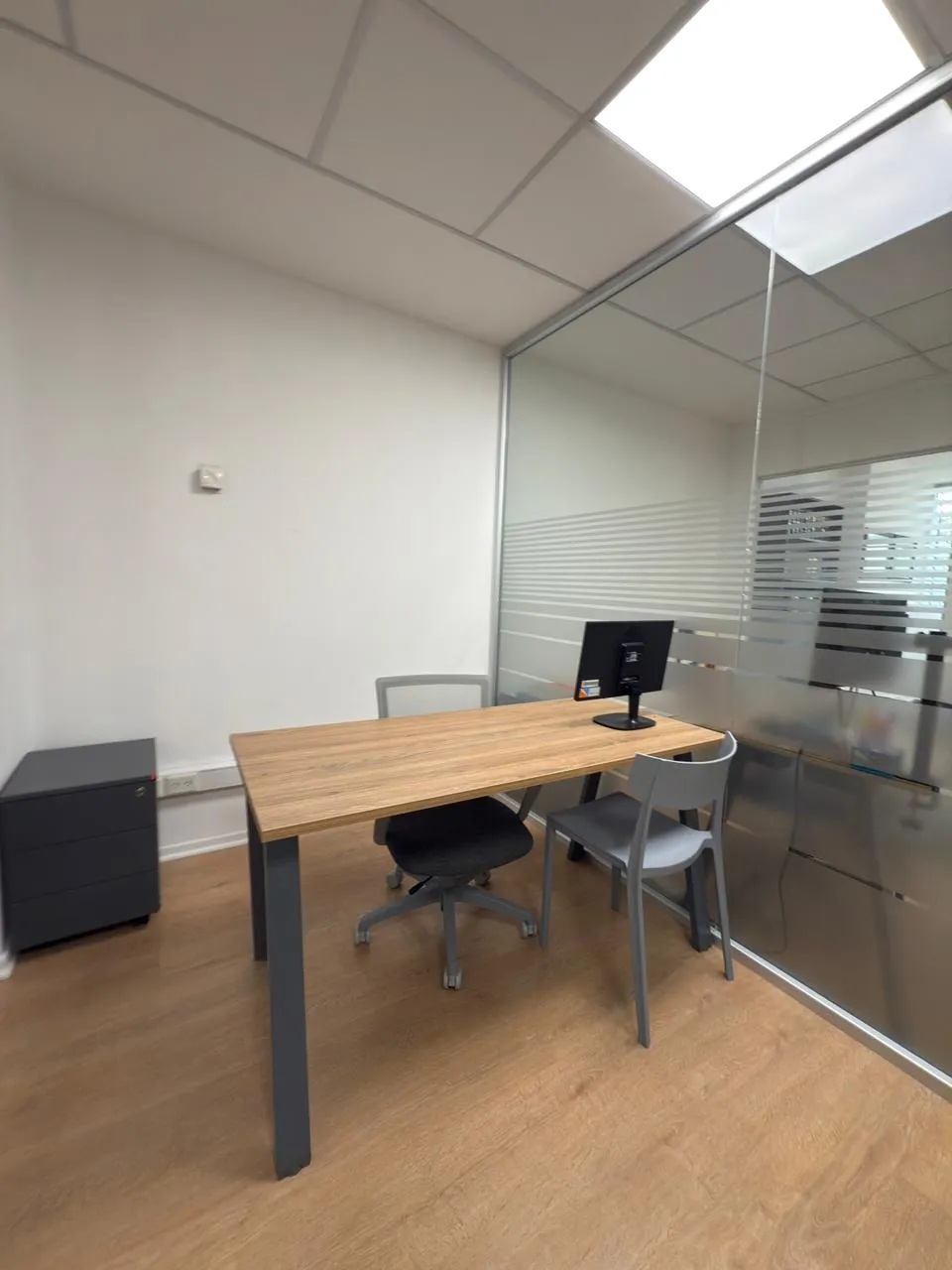 Puesto de trabajo individual con escritorio de madera y patas oscuras, monitor y silla ergonómica negra en oficina privada del Estudio Jurídico Inaudi.