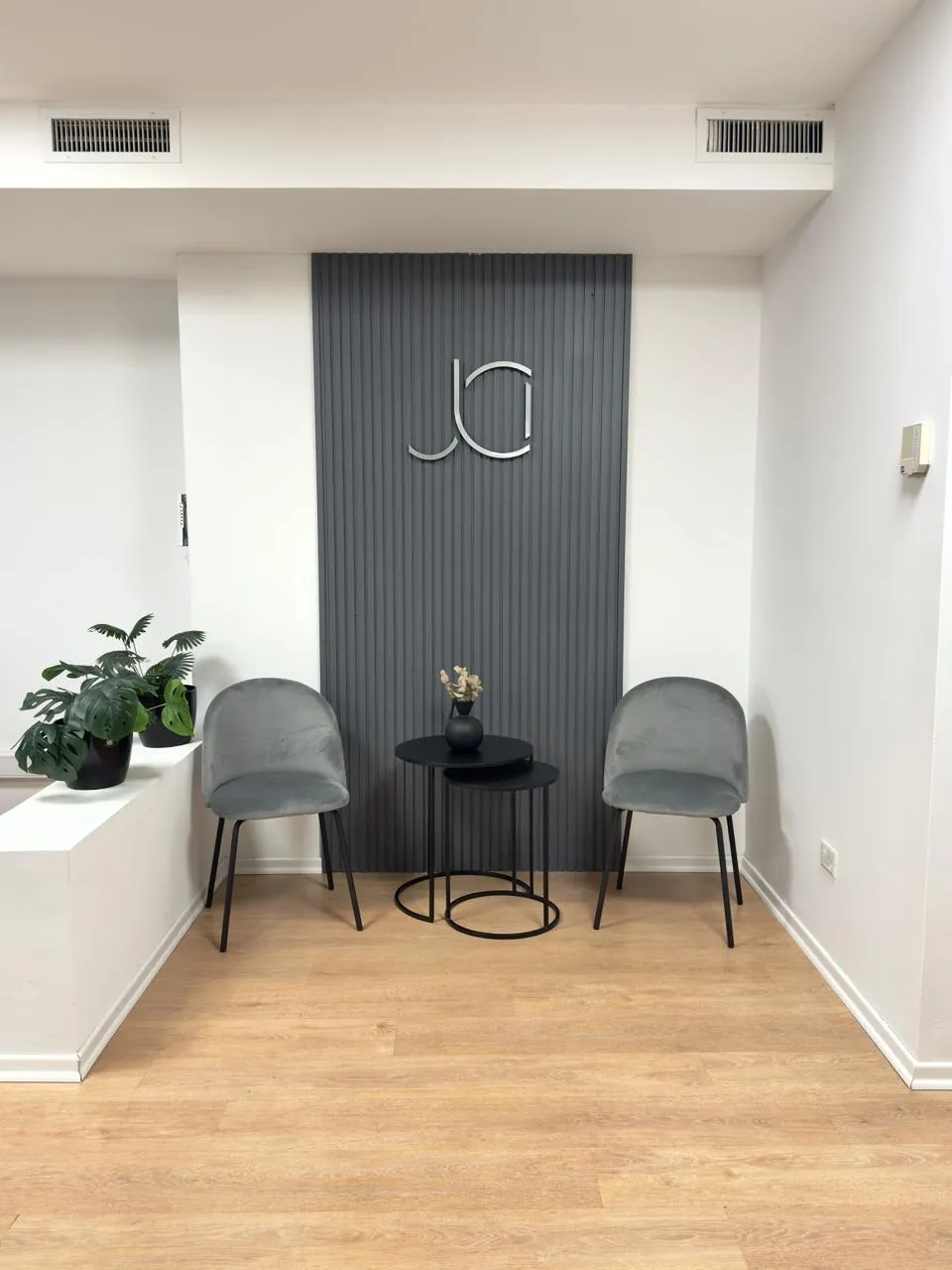 Sala de espera con dos sillas de terciopelo gris, mesas ratonas negras y logo del Estudio Inaudi sobre fondo de varillado gris.